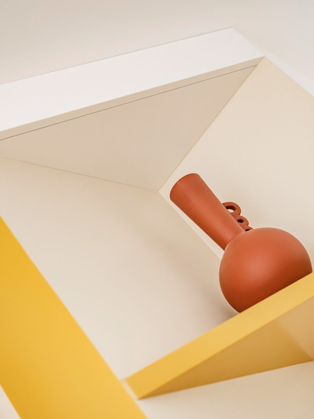 Vase en terre cuite posé sur une étagère jaune moutarde et blanche.