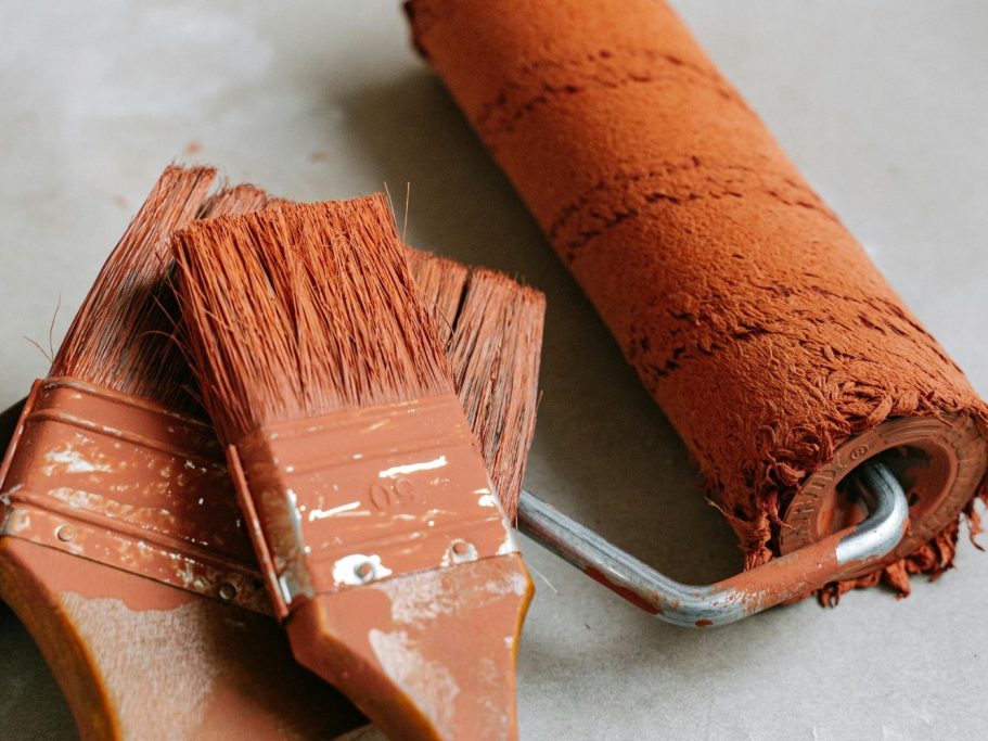 Rouleau et pinceau à peinture de couleur rouge ocre sur une surface grise.