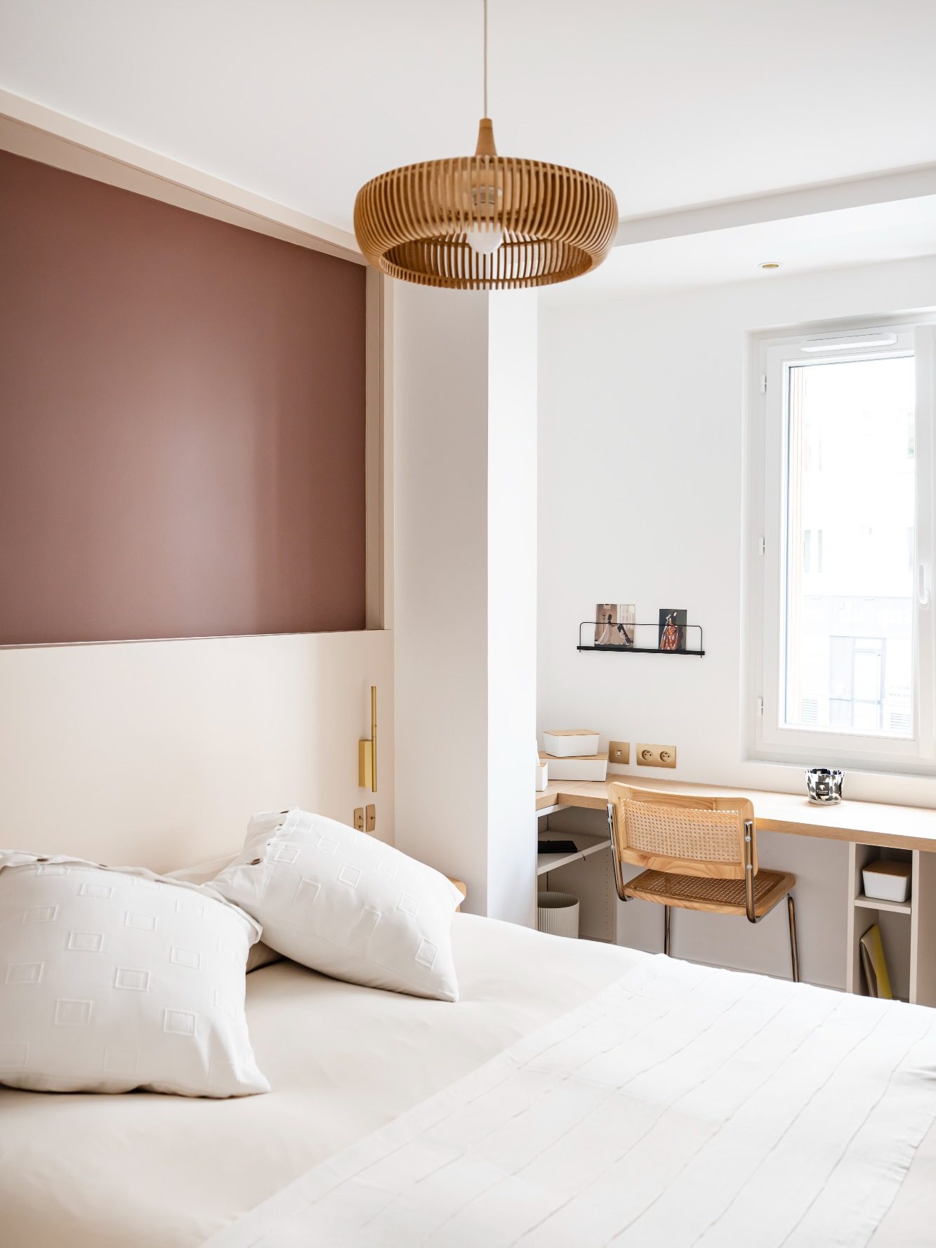 Chambre lumineuse avec un mur brun rosé, tête de lit sur mesure, lit et bureau en bois.