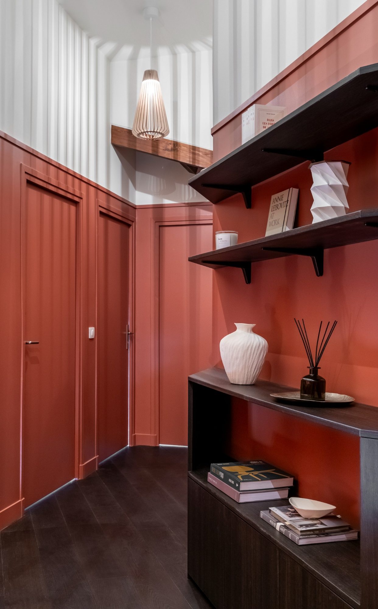 Dégagement moderne avec murs rouges, étagères en bois foncé et éléments décoratifs élégants.