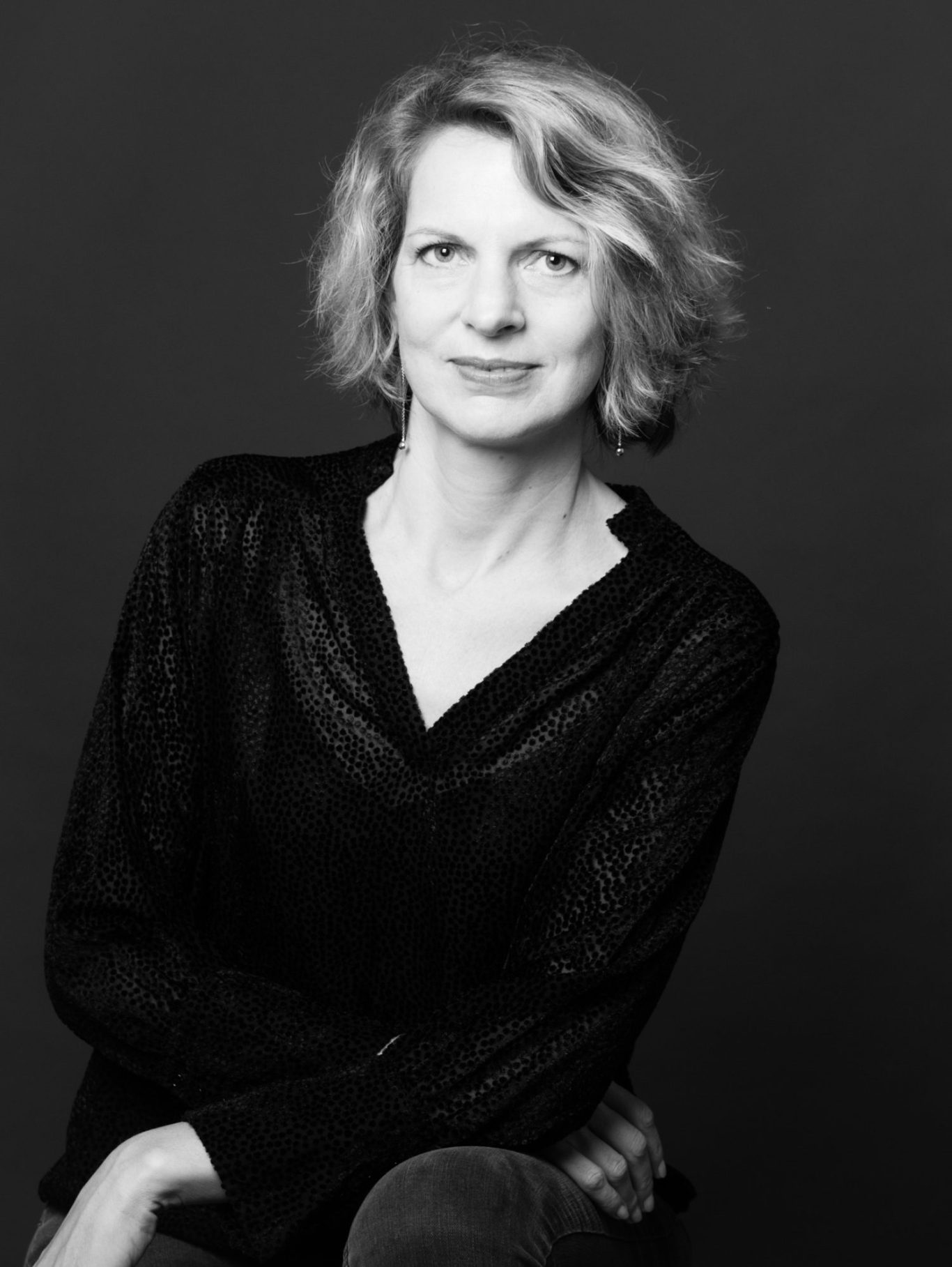 Portrait en noir et blanc d'Inès de Lacoste, une femme avec des cheveux blonds, souriante, vêtue d'un haut sombre.