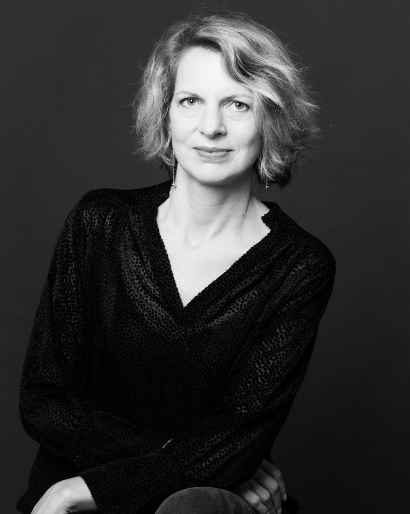 Portrait en noir et blanc d'une femme aux cheveux blonds, vêtue de noir, regard neutre.