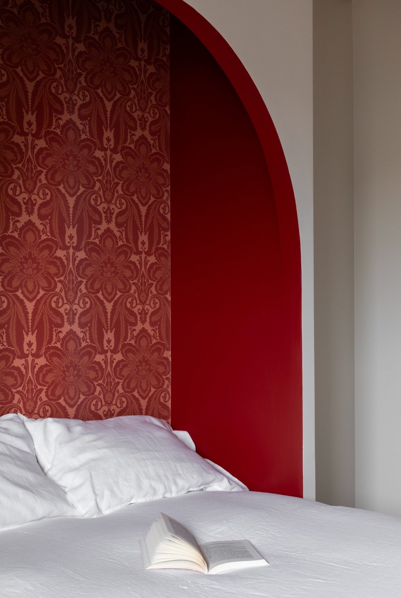 Lit dans une alcôve avec oreillers blancs contre un mur décoré d'un papier peint à motifs rouges.
