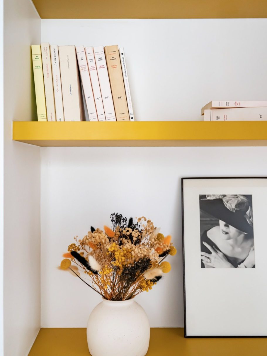 Une étagère moderne avec des livres, un vase de fleurs sèches et un cadre photo.
