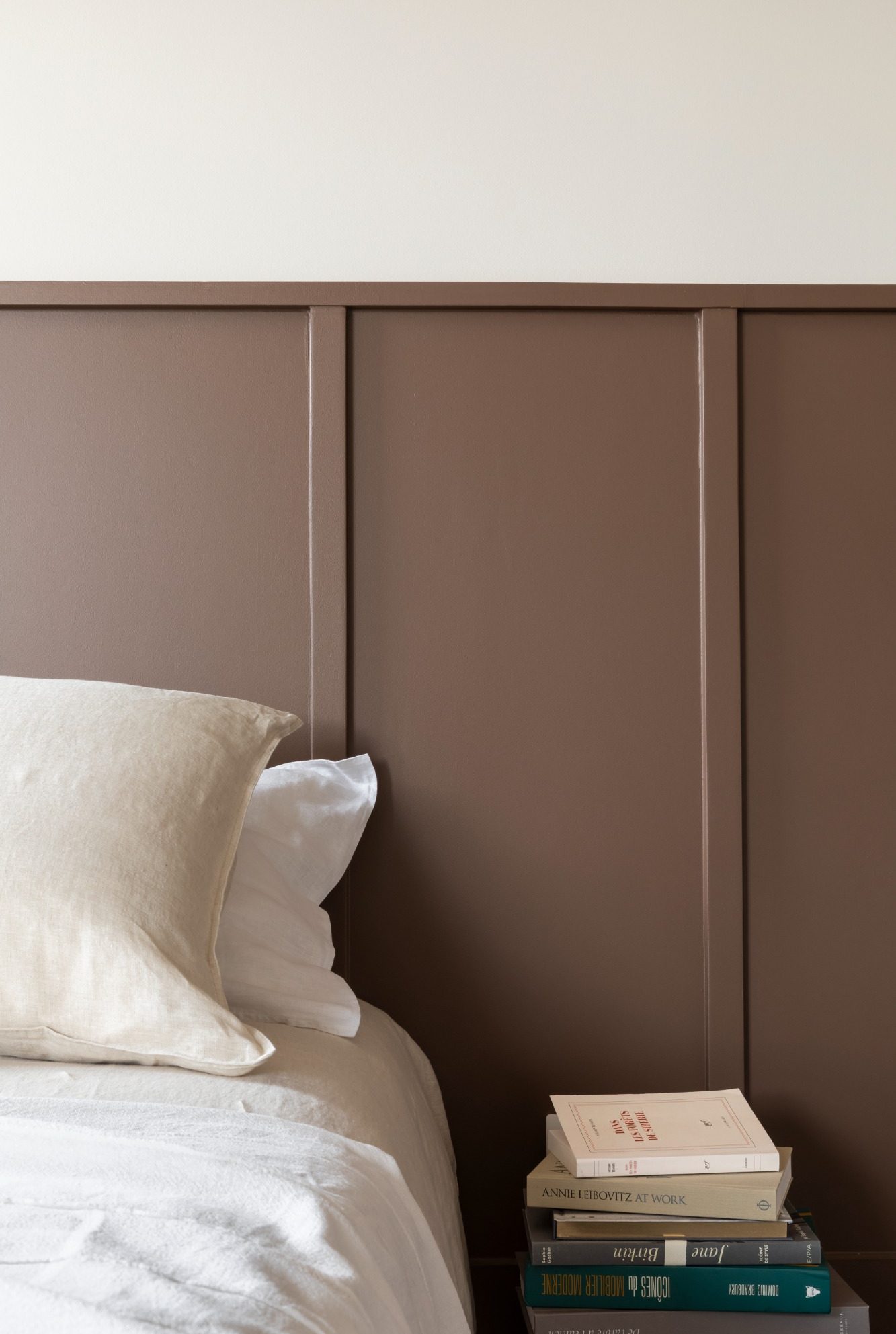 Lit avec une tête de lit marron et des livres empilés sur la table de nuit.