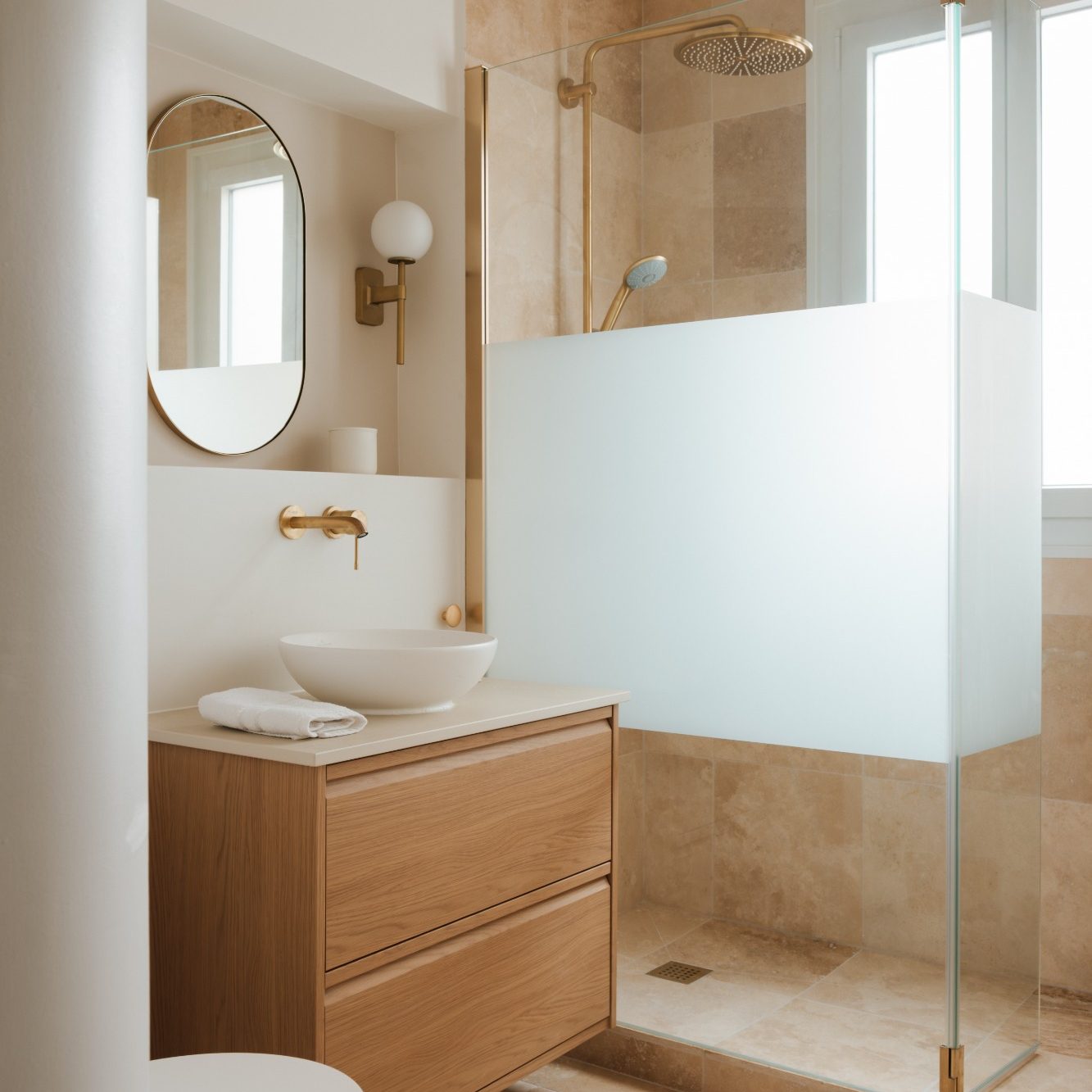 Salle de bain moderne avec douche vitrée, meuble vasque en chêne et sol en travertin.