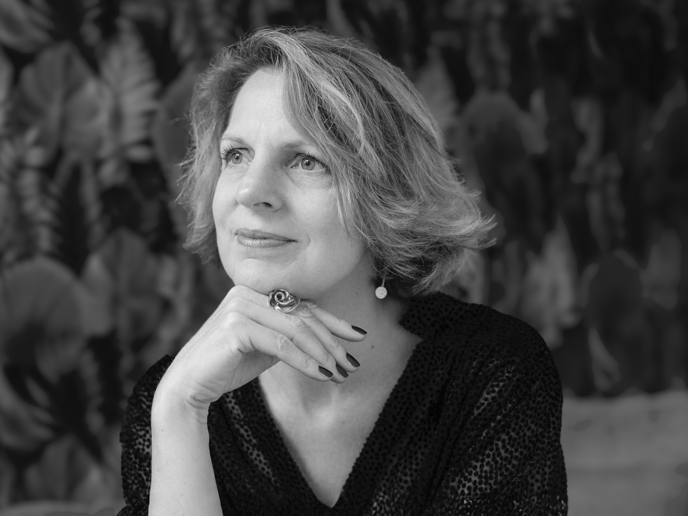 Femme pensant, mains sous le menton, avec un fond de feuillage.