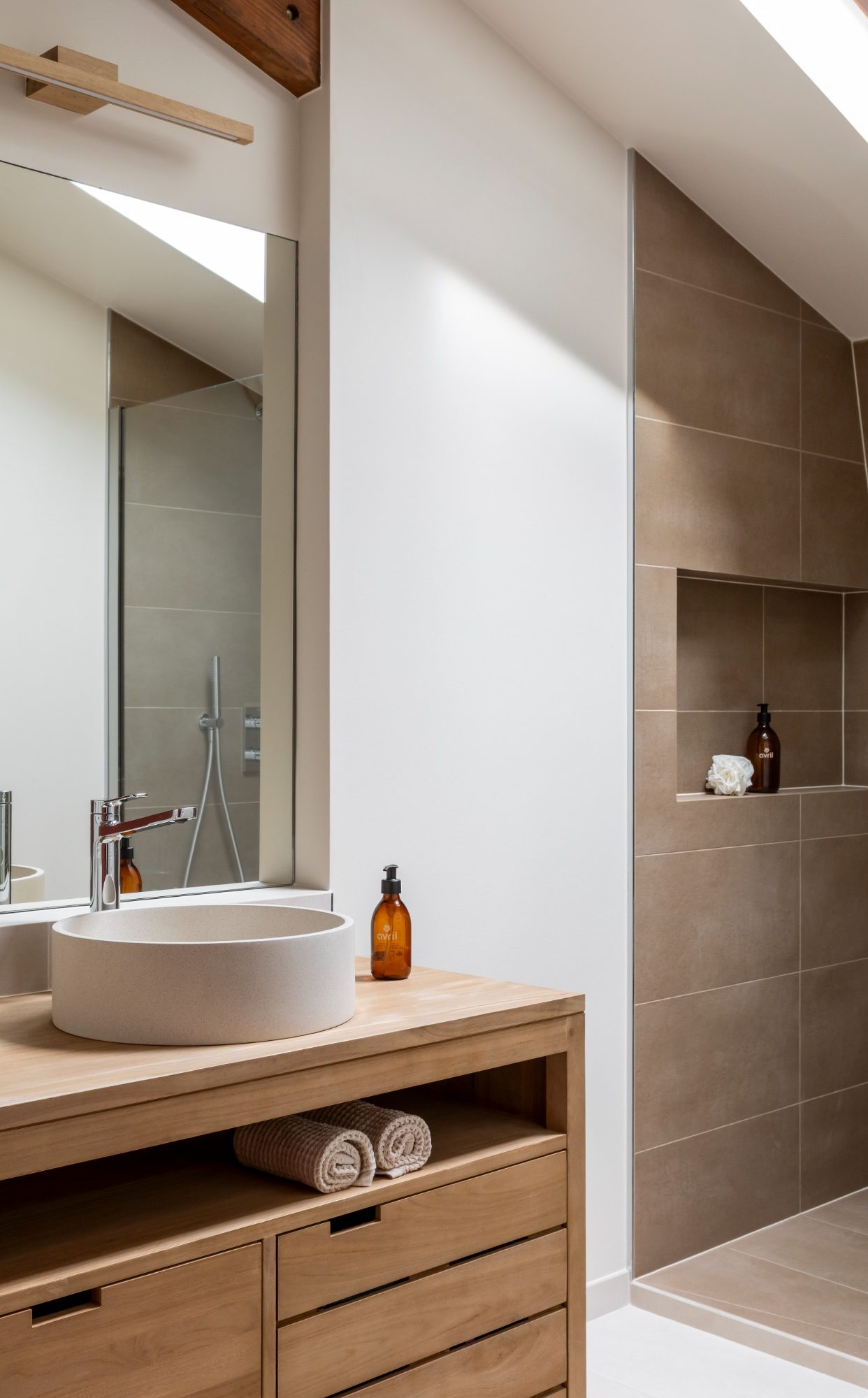 Salle de bain moderne avec un meuble vasque double en bois, douche ouverte et murs en carrelage clair.