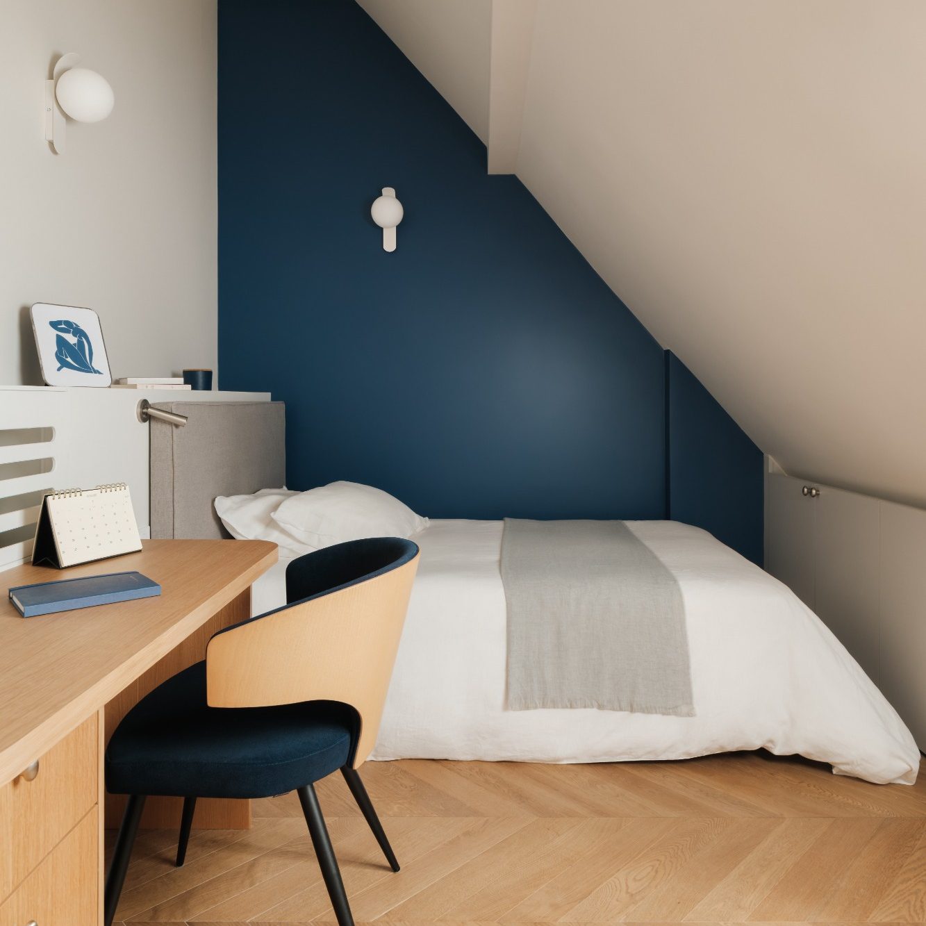 Chambre moderne en soupente avec mur bleu, lit, bureau en bois et chaise.