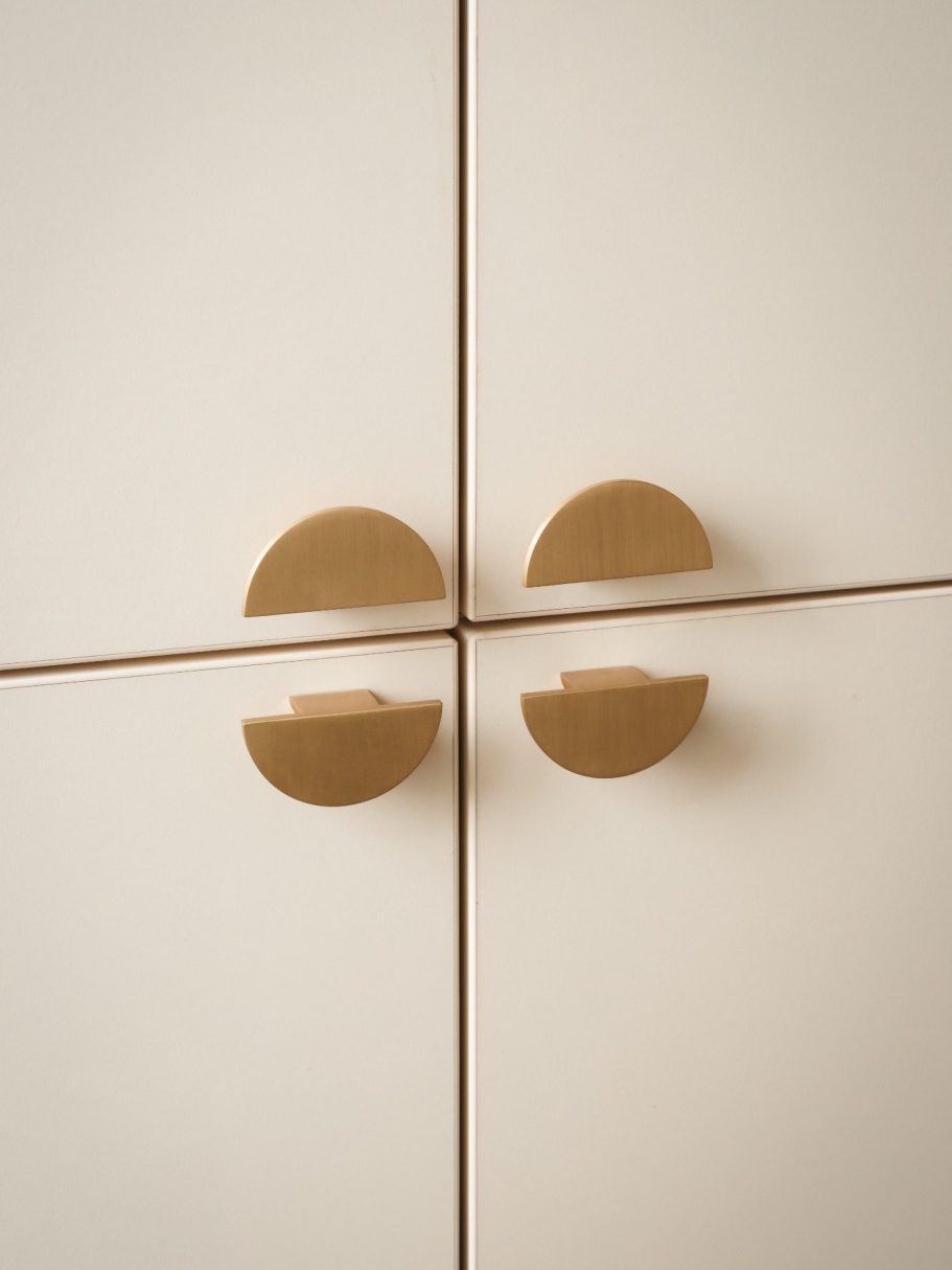 Jeu de symétrie avec des poignées dorées en forme demi-cercle sur des portes de placard crème.