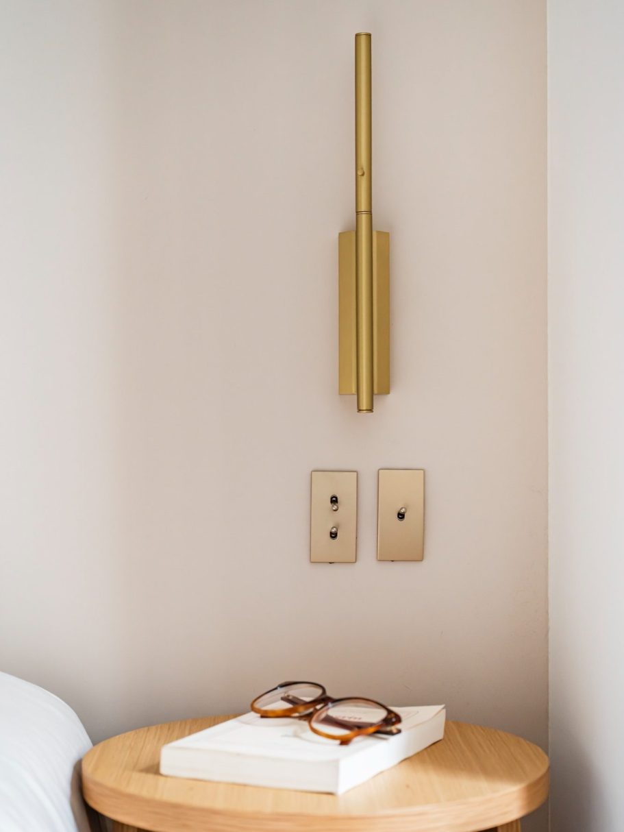 Applique murale dorée à côté d'interrupteurs et de lunettes sur une table en bois.