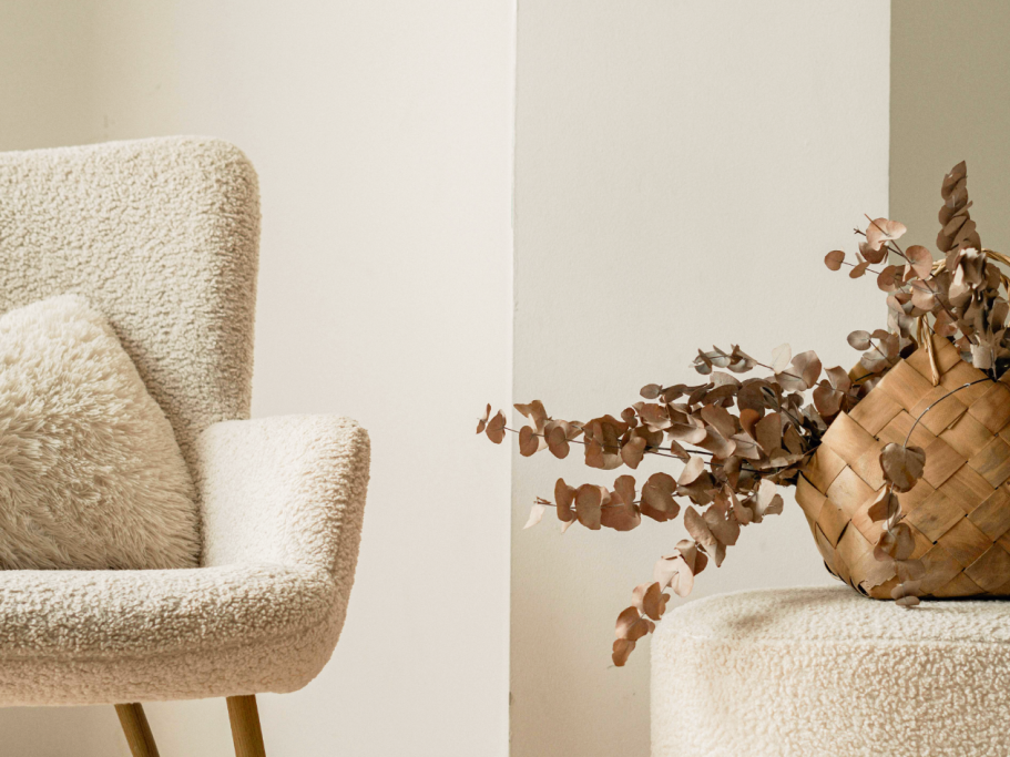 Fauteuil en tissu beige avec coussin et vase en osier, contenant des fleurs sèches.