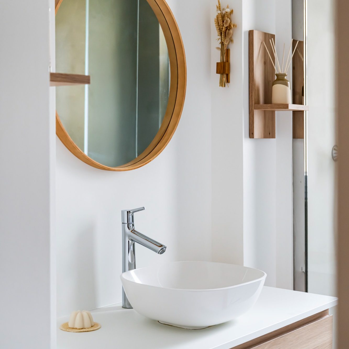 Salle de bain moderne avec lavabo rond, miroir circulaire et étagères en bois.