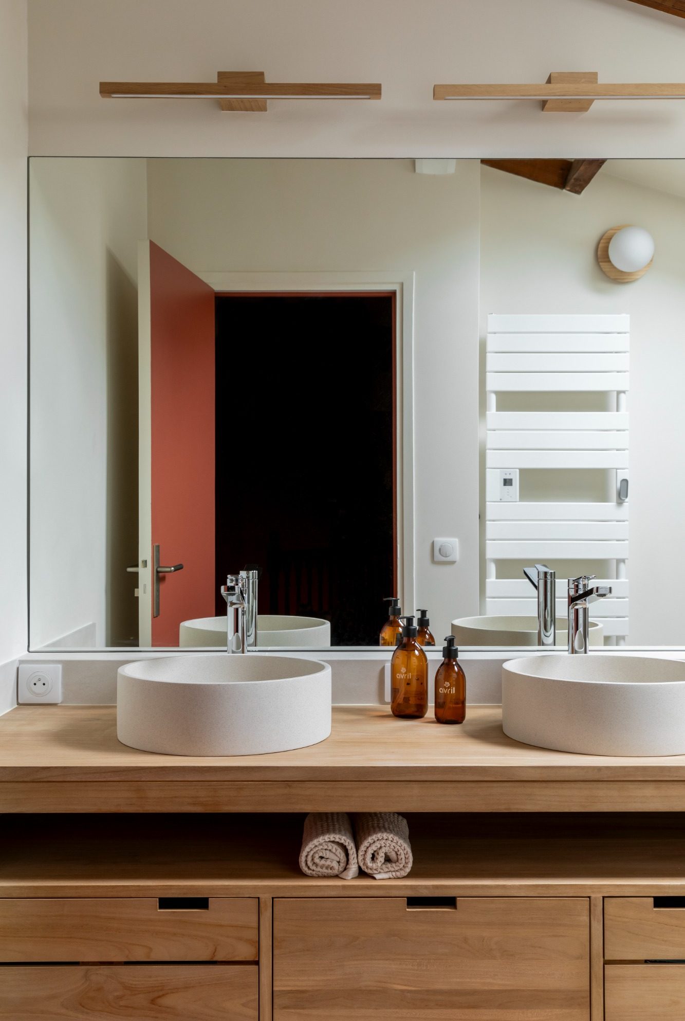 Salle de bains avec meuble vasque double, vasques à poser rondes, miroir, décor minimaliste et moderne.