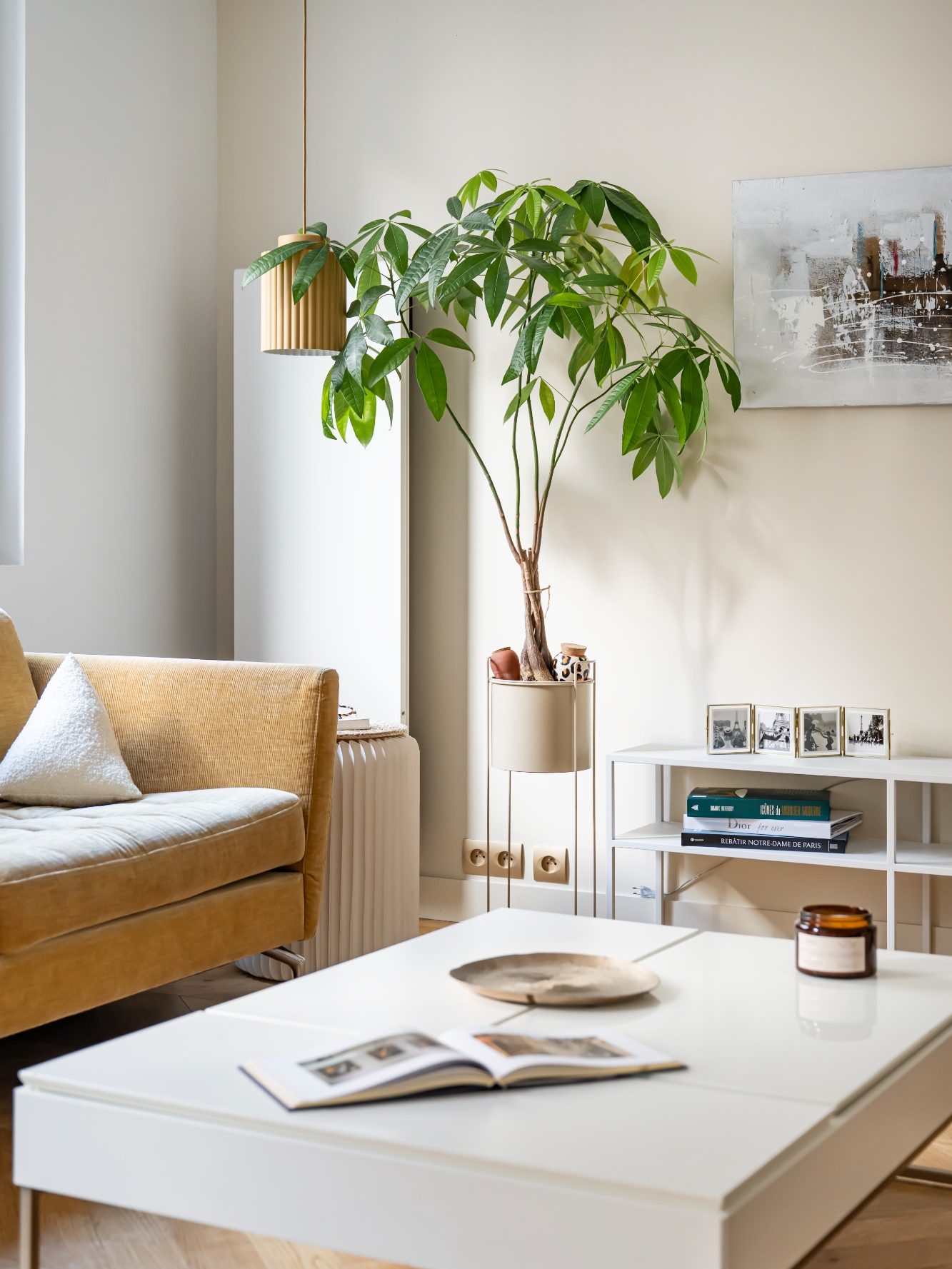 Salon moderne avec un canapé jaune moutarde, une table basse, une plante verte et des objets décoratifs.