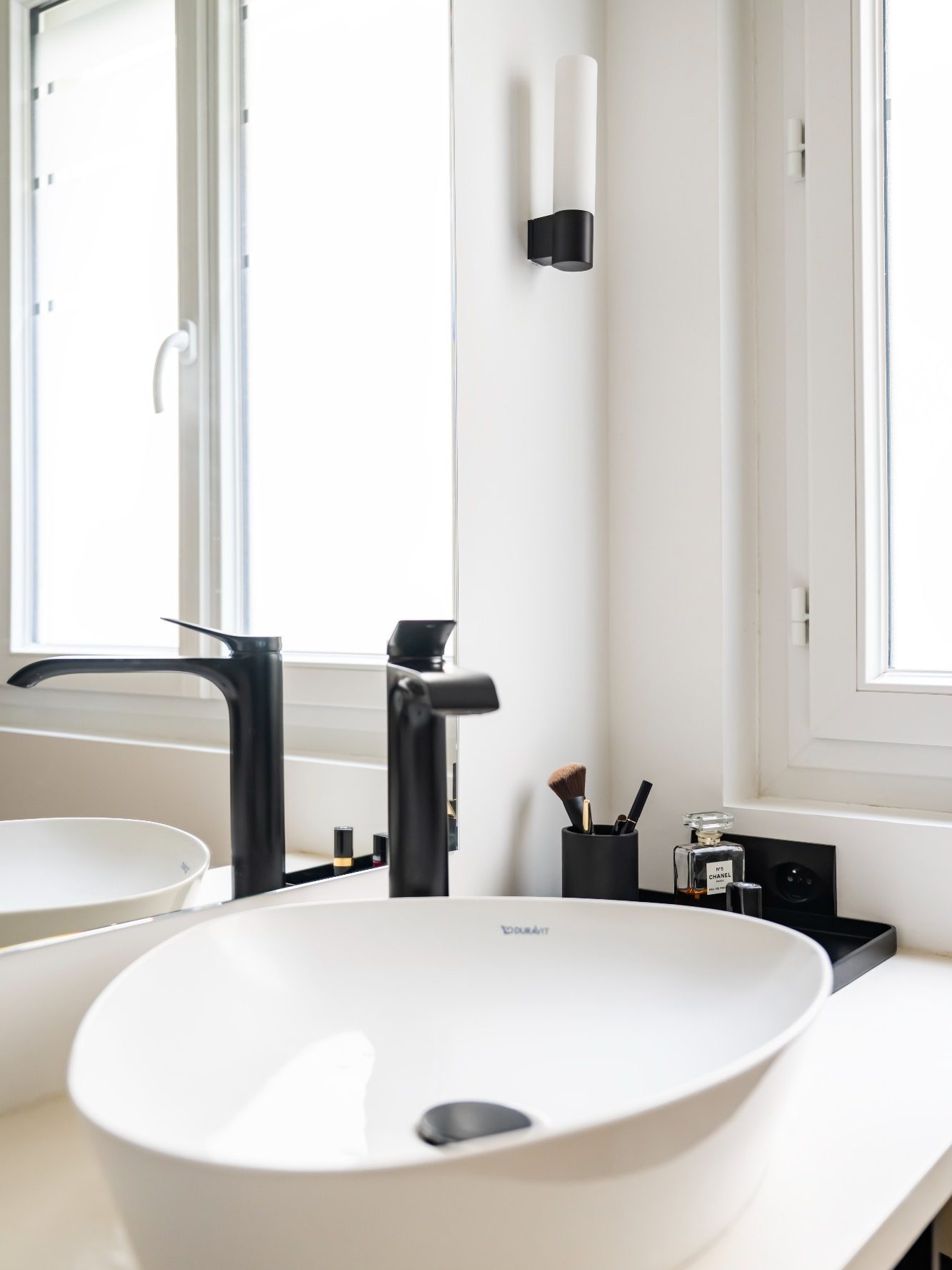 Vasque blanche moderne avec robinet noir, lumière naturelle et accessoires sur le plan vasque.