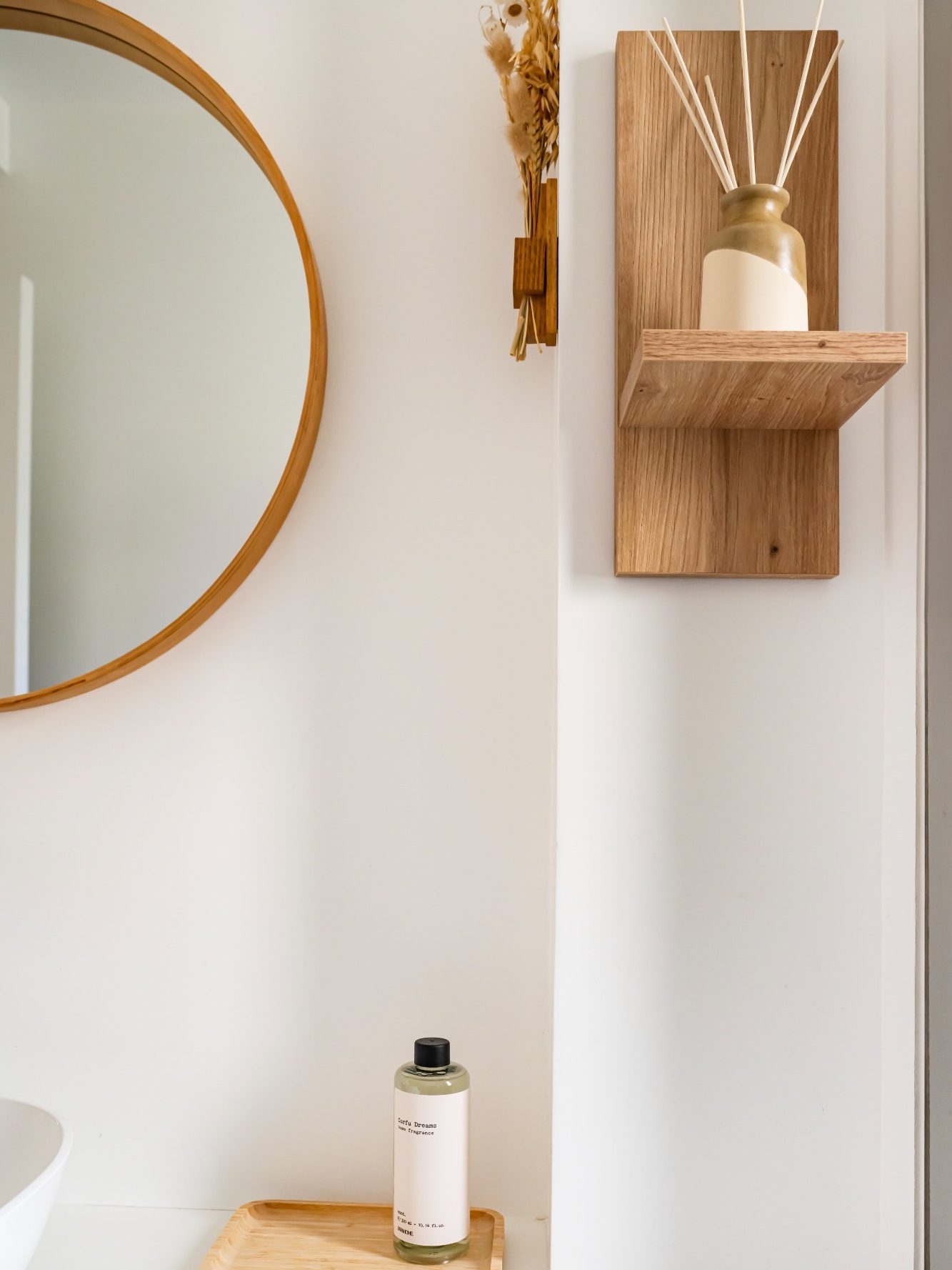 Miroir rond et étagère en bois avec un diffuseur et un flacon sur un meuble.