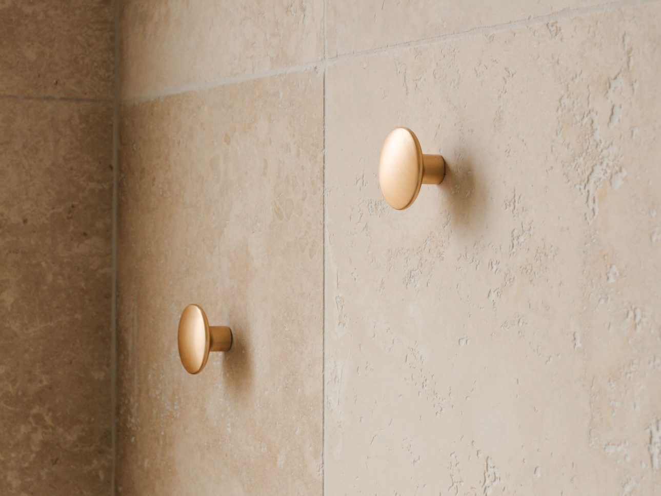 Deux crochets muraux en métal doré sur un mur beige.