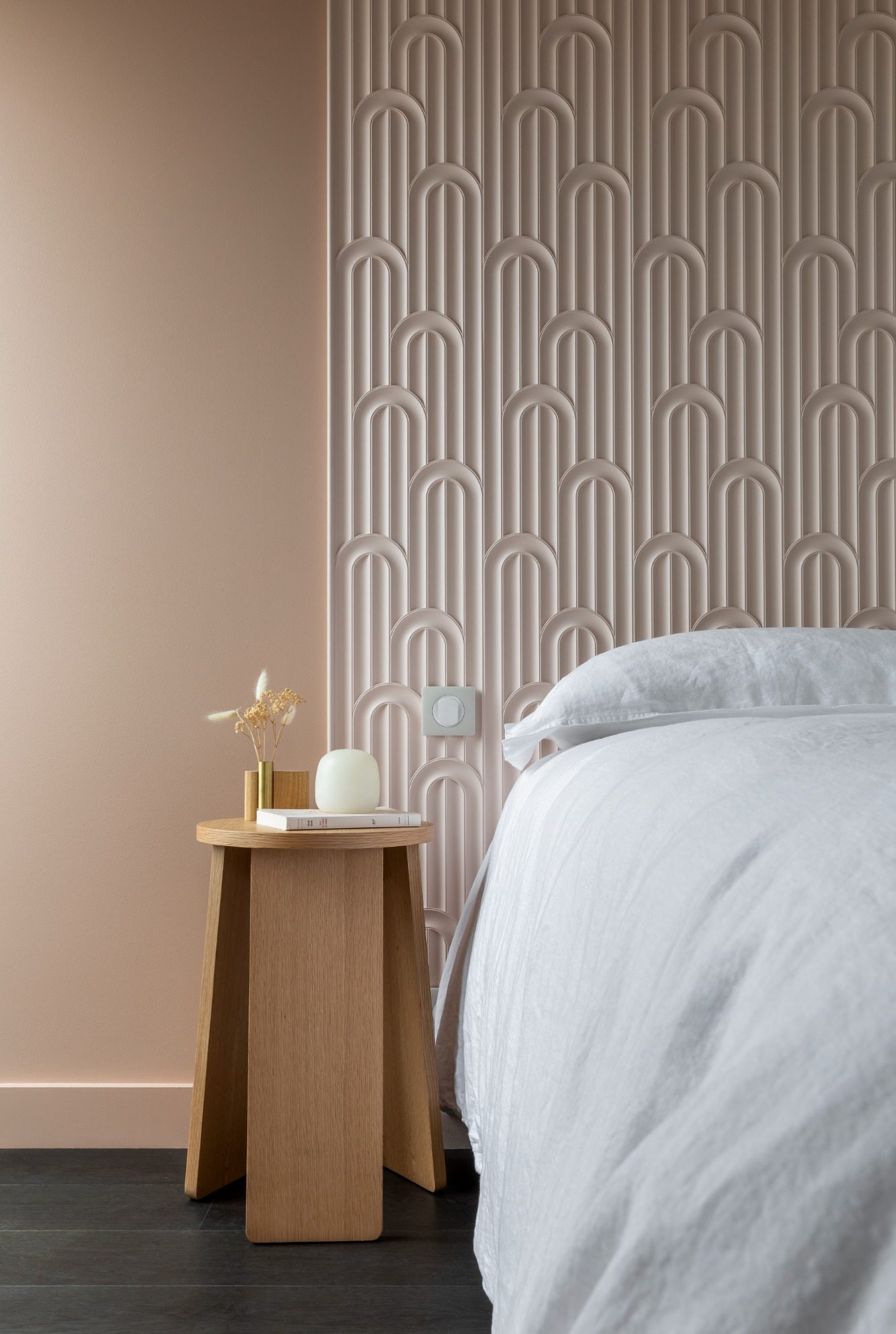 Chambre moderne avec un mur texturé rose et une table de nuit en bois.
