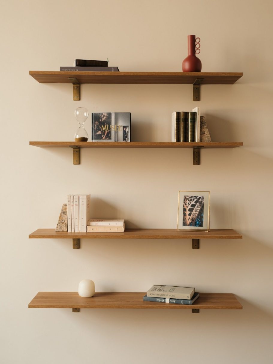 Étagères en bois avec livres, vases et un bougeoir sur un mur beige.