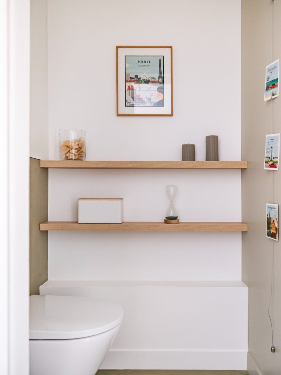 Toilettes modernes avec étagères en bois, décoration murale et sol en béton ciré