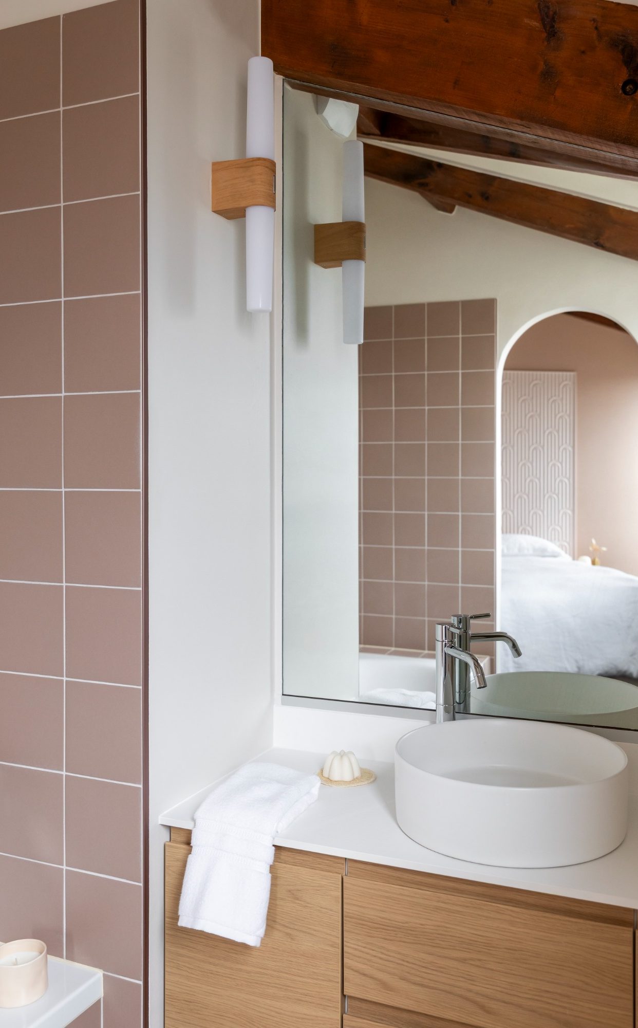 Salle de bain moderne avec carrelage rose, miroir, lavabo rond et éléments en bois.