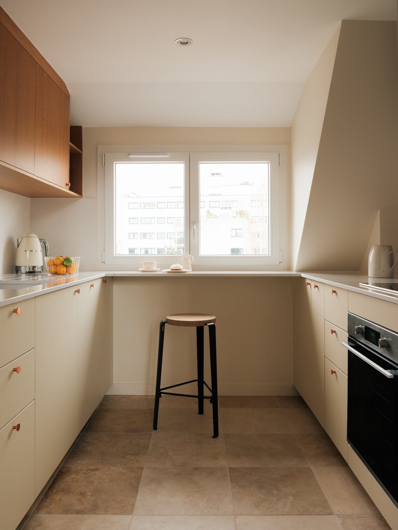 Cuisine moderne sur mesure chêne et crème, plan bar et son tabouret, plan de travail Silestone, sol en travertin et fenêtre lumineuses