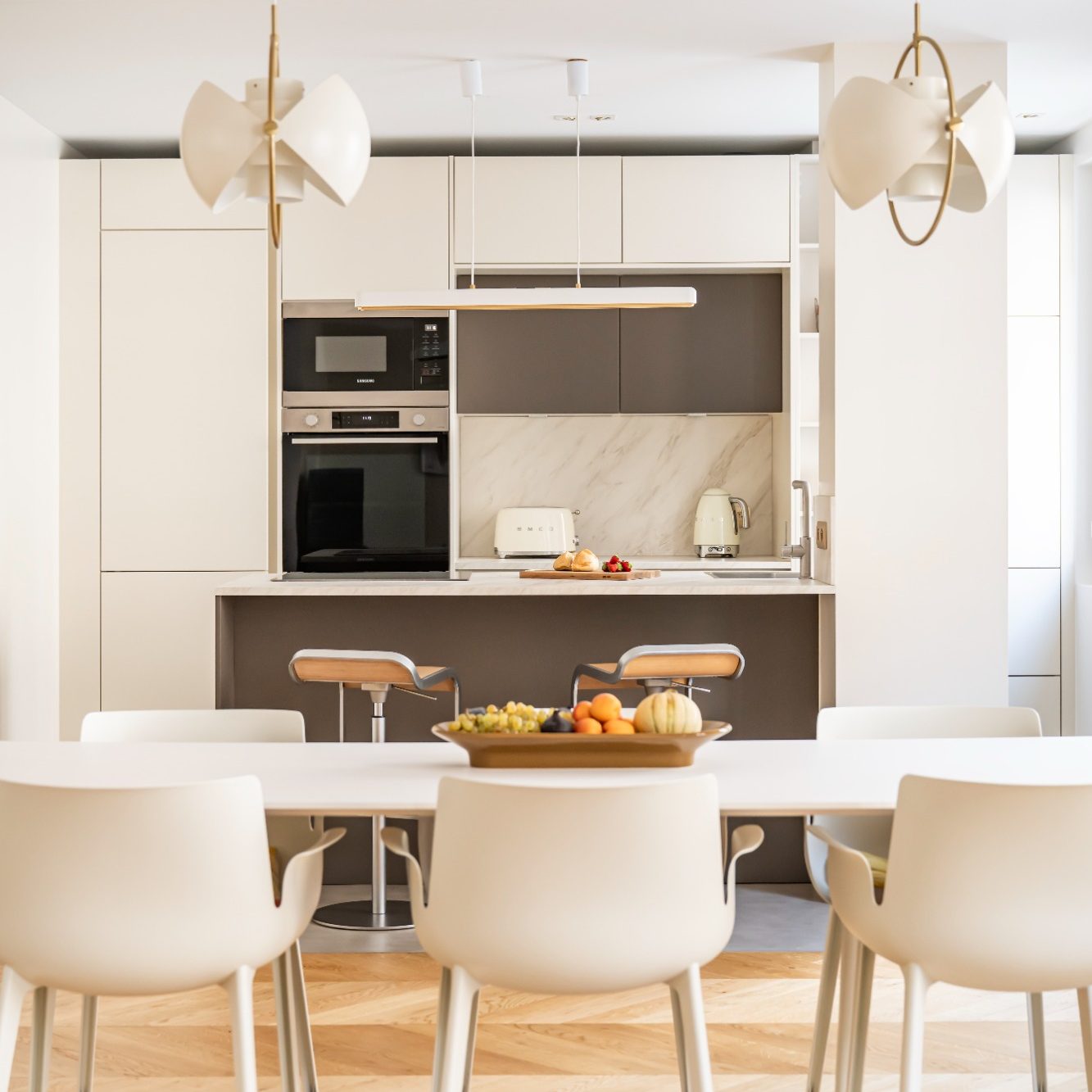 Cuisine moderne et lumineuse avec table à manger, chaises blanches et appareils intégrés.