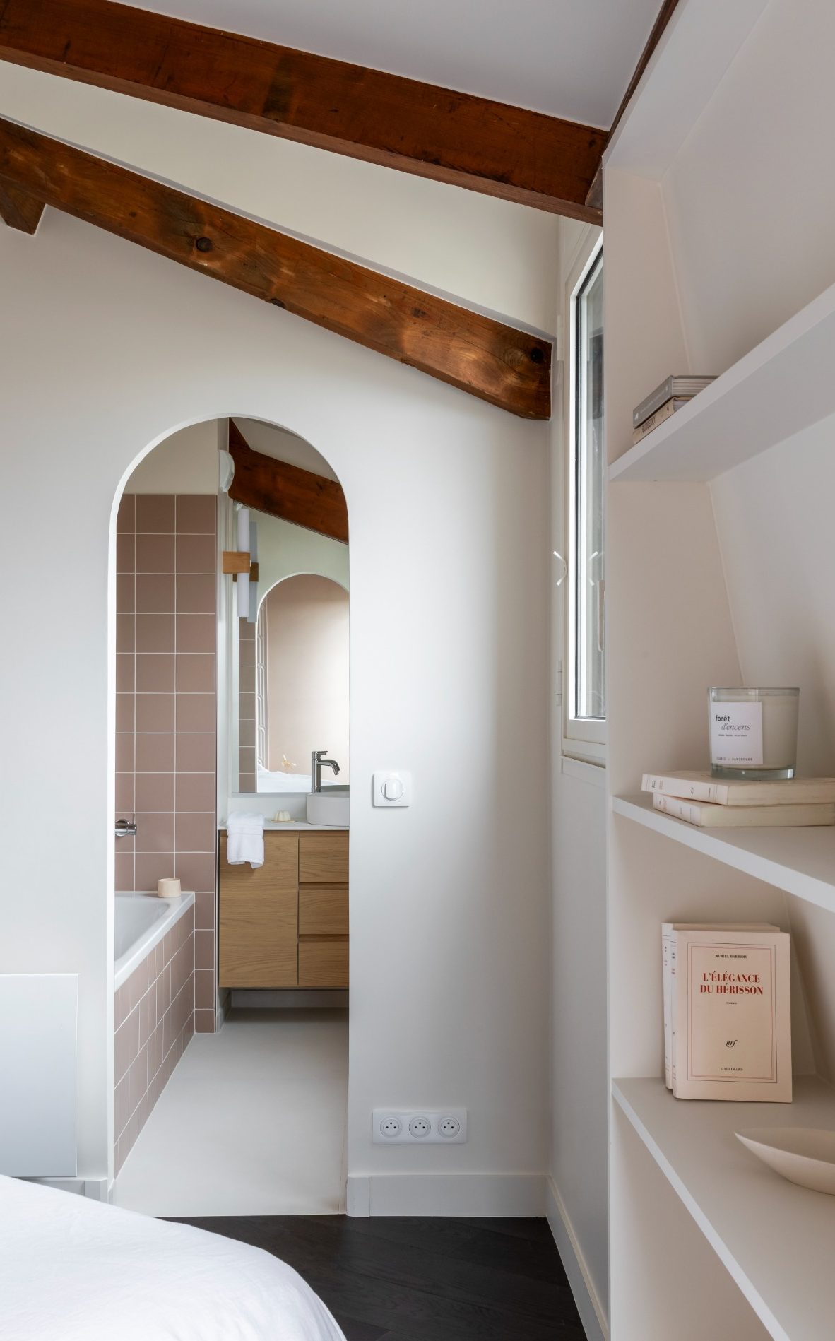 Chambre lumineuse avec salle de bains en arrière-plan et meuble vasque en bois.