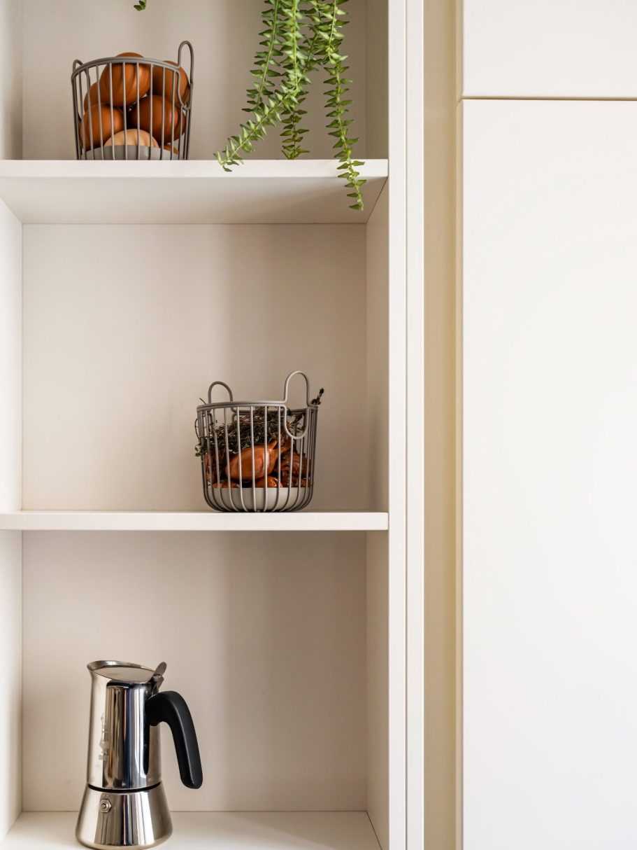 Etagères ouvertes de cuisine avec plante, deux paniers en métal contenant des oranges et une cafetière.