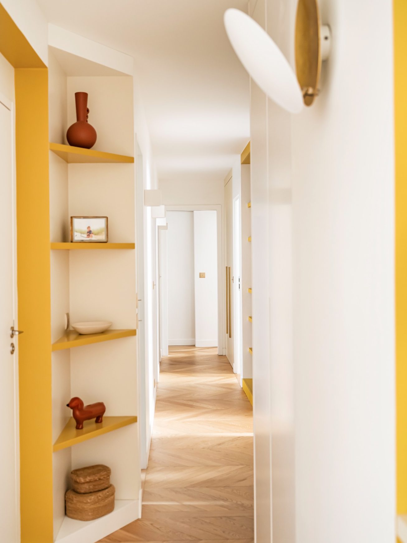 Couloir lumineux avec étagères jaunes moutarde, décoré d'objets en terre cuite et bois.