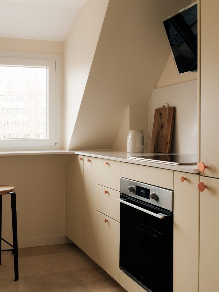 Cuisine moderne avec armoires claires, four en-dessous et fenêtre apportant de la lumière.