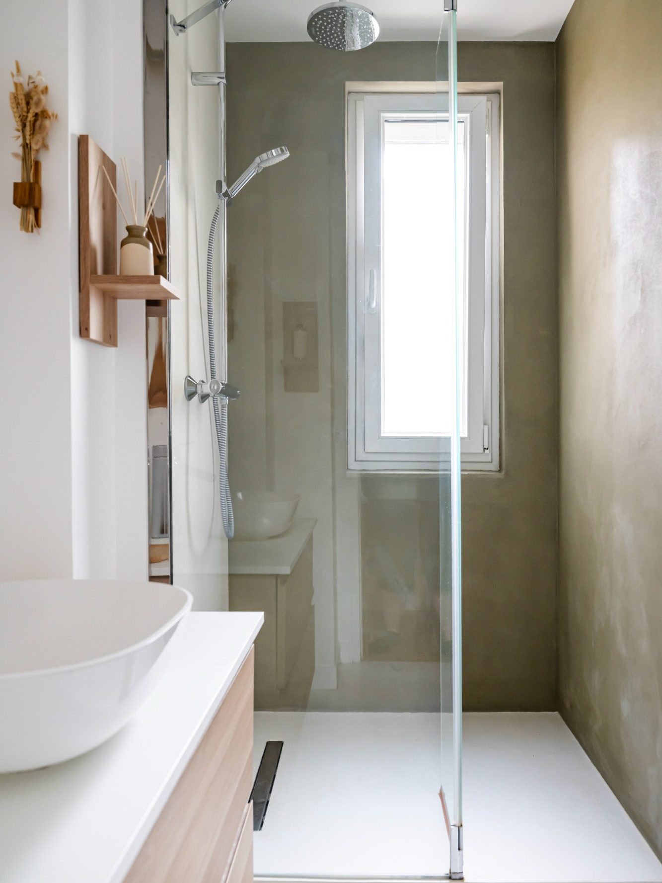 Salle de bain en béton ciré avec douche vitrée et murs aux teintes naturelles.