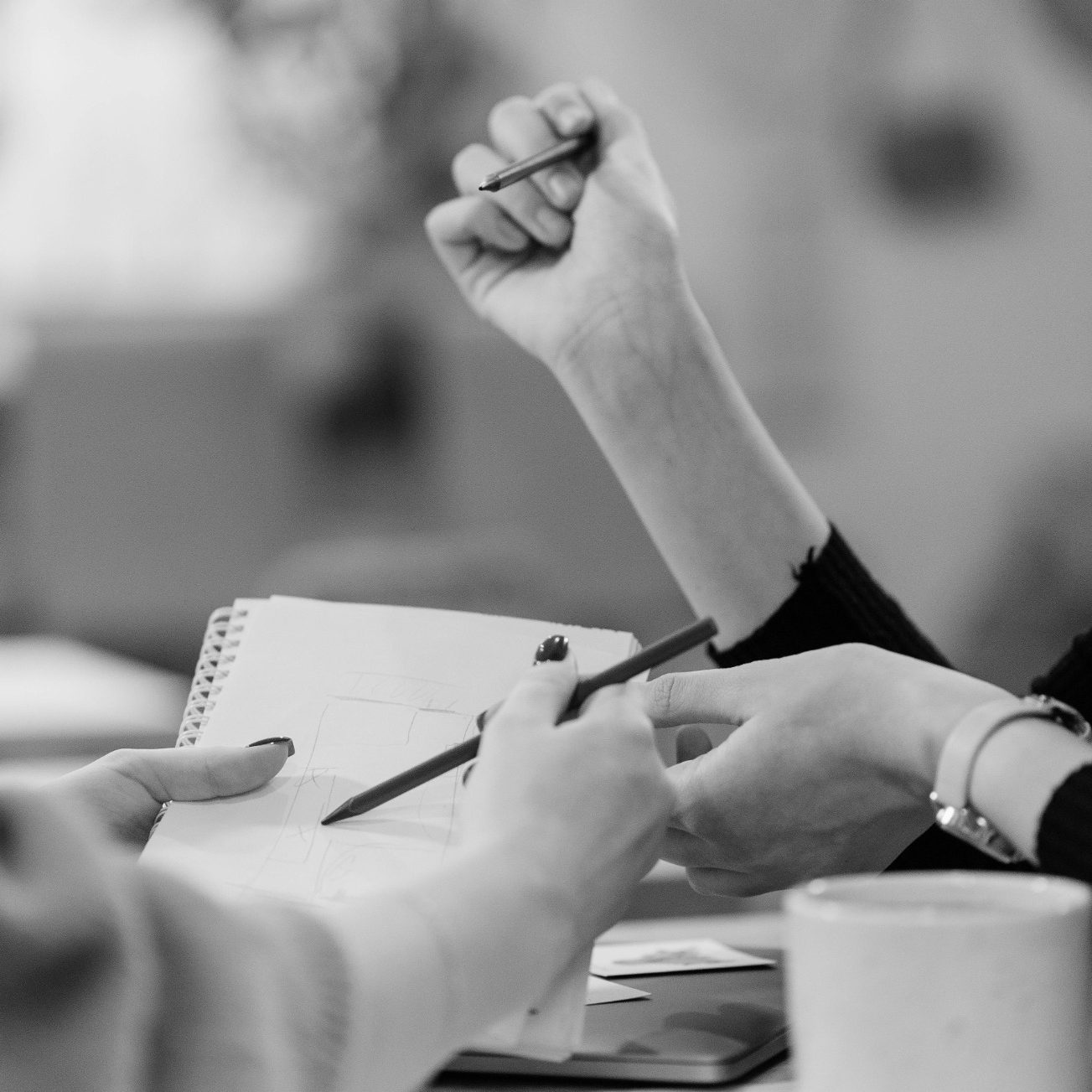 Deux mains se rencontrent, l'une tenant un stylo, l'autre un carnet. Ambiance floue.