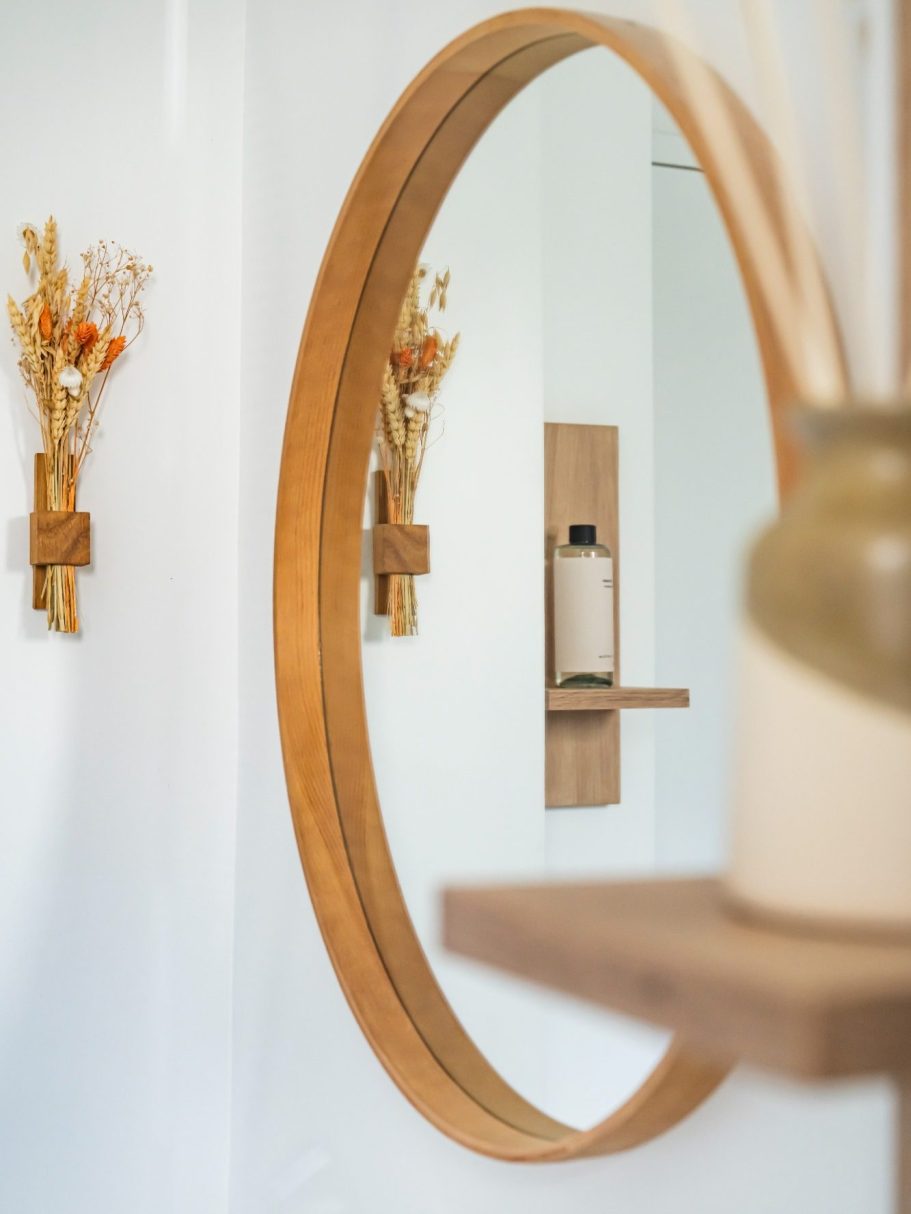Miroir rond en bois avec des décorations florales et un flacon sur un support.