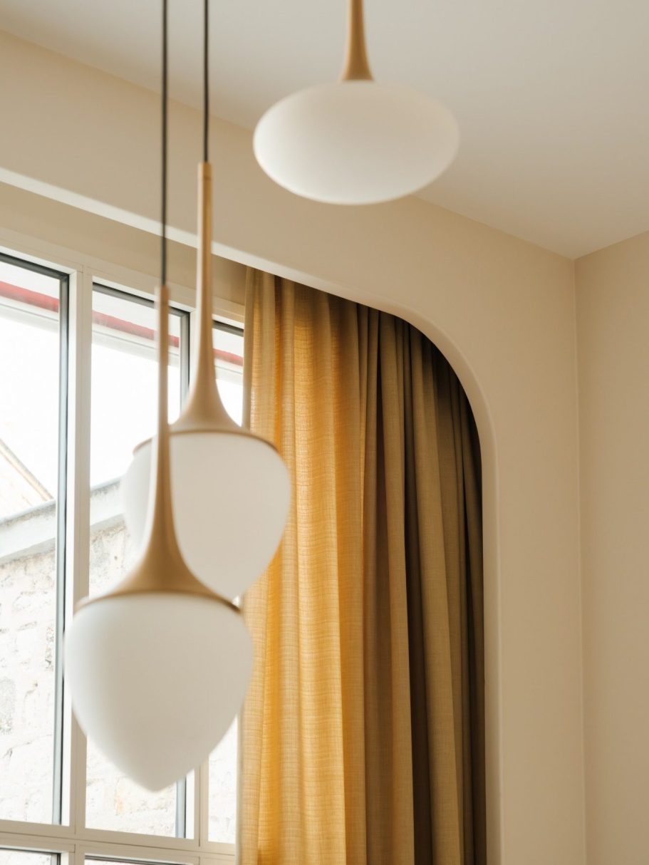 Lustre avec triple suspensions opales et laiton, avec rideaux jaunes moutarde dans un intérieur moderne.