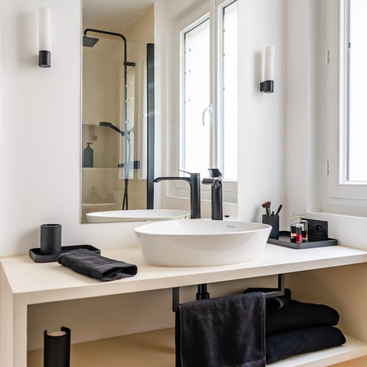 Salle de bain moderne avec lavabo rond, serviettes noires et douche vitrée.