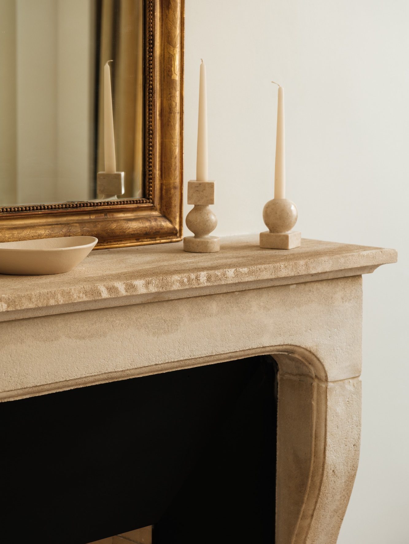 Cheminée en pierre avec bougeoirs en bois et miroir doré en arrière-plan.